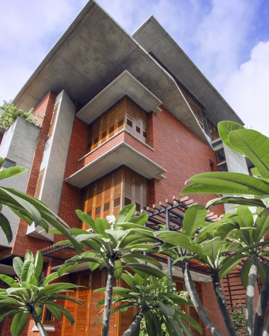 Looking up at a brick and concrete building with timber shutters behind frangipani trees
