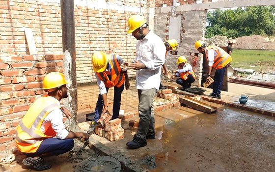 Site team in hard hats and safety vests laying bricks on a construction site